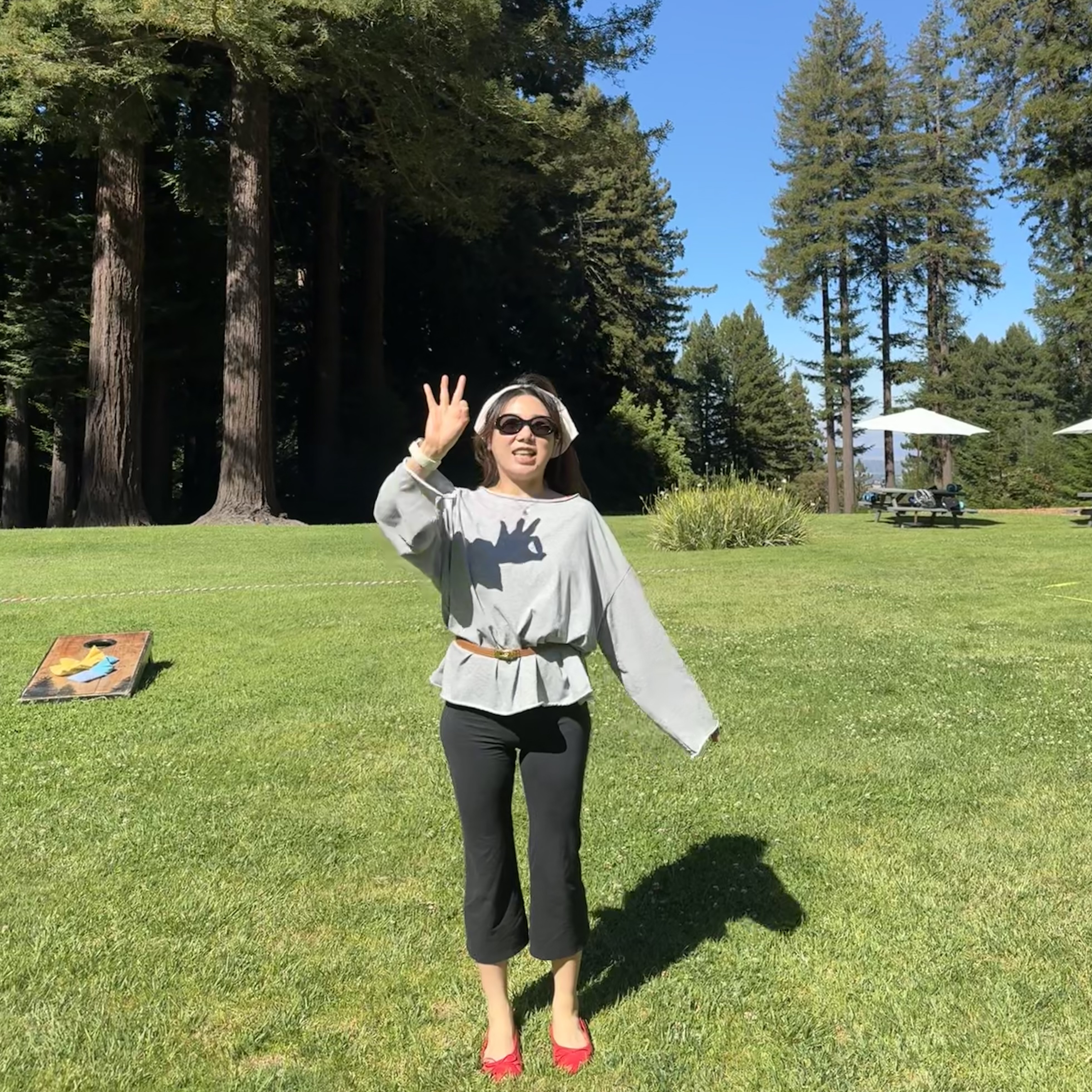 Alina Xie outdoors at a redwood park, making a peace sign